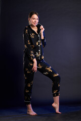 A woman in a black and gold pajama set poses for the camera in a studio against a dark background. The outfit features animal prints, giving it a playful and whimsical look. Confident pose of a woman