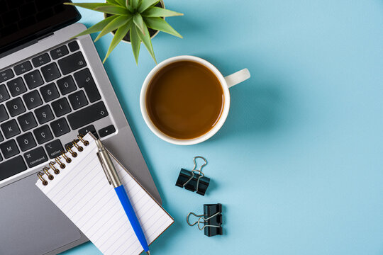 Coffee cup, laptop keyboard and various stationery items on blue office desk. Business office concept