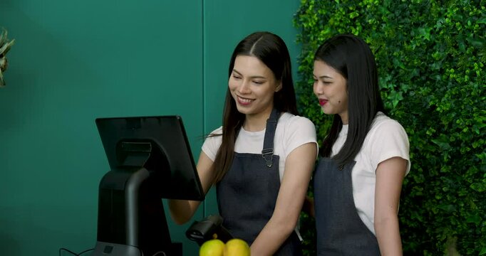 Asian women smiling while using a monitor at the shop counter to finalize fruit orders. Demonstrates customer-centric service, digital integration, and efficient teamwork in small business operations.