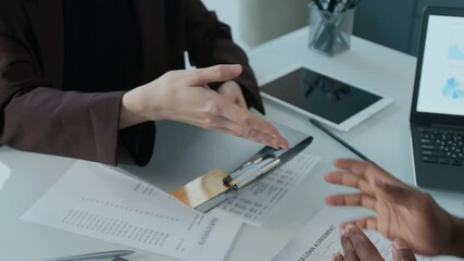 Close up view of financial advisor giving credit card and related documents on clipboard to female client, then shaking her hand during consultation