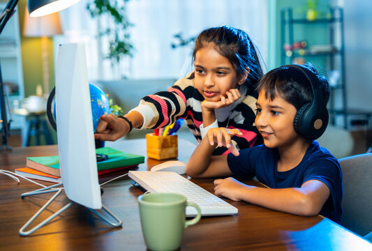Indian kids using a laptop, working on homework together, sharing, learning in a cheerful home setup