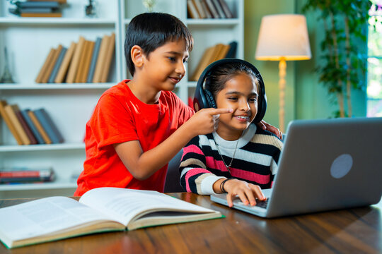 Indian kids using a laptop, working on homework together, sharing, learning in a cheerful home setup