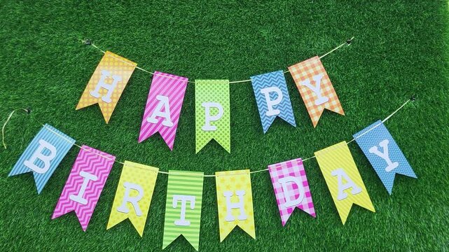 Colorful "Happy Birthday" bunting with patterned flags on green grass background. Overhead composition. Birthday celebration concept. Design for banners, greeting cards, and party invitations.