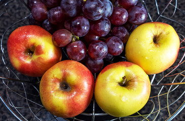 Close-up of four garden apples and branches of red grapes in a metal vase, half-cropped image, top view.