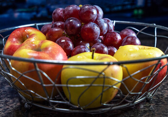 Close-up of four garden apples and branches of red grapes in a metal vase, side view.