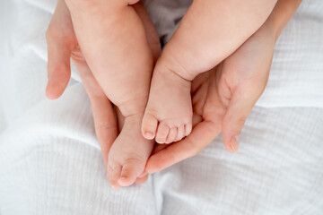 mom's hands hold the legs of a newborn baby, legs in focus, pink baby heels