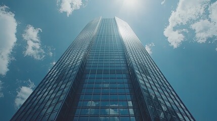 Fototapeta premium A modern skyscraper reaching towards a bright sky with fluffy clouds.