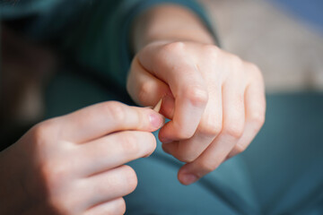young girl's hand delicately cares for her nails using an orange wood stick, showcasing a moment of personal grooming and self-care