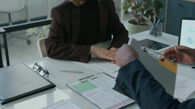 Tilt up shot of young woman handing document to financial advisor, receiving file with credit card and papers and shaking his hand during consultation in office