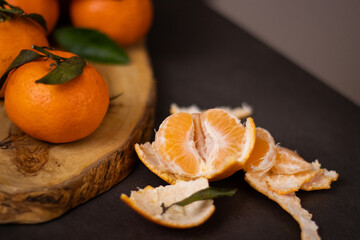 Close up of peeled mandarine slices and a pile whole mandarines on wooden plate, blurry green pine...