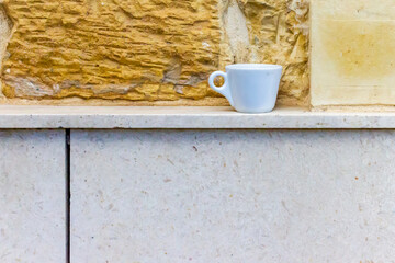White Espresso Cup on Stone Ledge Against Textured Wall Background