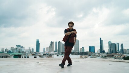 Motion shot of B-boy dance performance by professional street dancer at rooftop with sky scrapper, city view. Attractive asian hipster show energetic footstep. Outdoor sport 2024. Hiphop.