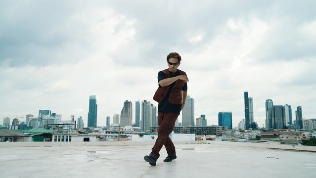 Motion shot of B-boy dance performance by professional street dancer at rooftop with sky scrapper, city view. Attractive asian hipster show energetic footstep. Outdoor sport 2024. Hiphop. - Powered by Adobe