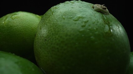 Slices of lime are meticulously arranged in a pile, set against a black background. Each lime slice is captured in stunning detail, its vibrant green hue and enticing texture. Close up. Comestible.
