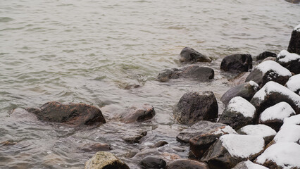 Snow Covers Rocks Along the Shoreline While Water Gently Laps at the Stones in a Tranquil Winter Setting