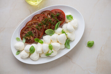 Plate with sliced tomatoes and mini mozzarella balls, horizontal shot on a beige granite background, high angle view