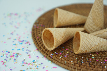 five empty ice cream cones lying on a rustic brown base with colorful sprinkles, isolated on white background