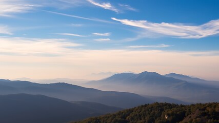 Serene panorama of misty mountain ranges under a tranquil blue sky with wispy clouds at dawn or dusk, ideal for nature and travel photography