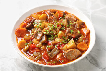 Delicious stew with vegetables in bowl on white marble table, closeup