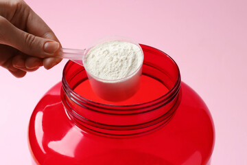 Woman taking scoop of protein from jar on pink background, closeup