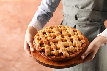 Woman holding wooden board with tasty homemade apple pie on light coral background, closeup
