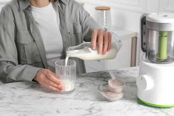 Making protein cocktail. Woman pouring milk from bottle into glass at white marble table, closeup