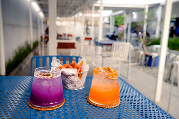 Fresh iced purple butterfly pea and orange soda drinks and fried sausages served on blue perforated steel plate table in an empty restaurant