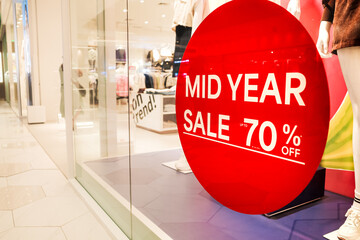 Red 70 Percent Mid Year Sale Sign Sticker on Display Window Near Fashion Clothing Store Entrance in...