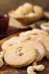 Tasty cashew cookies with powdered sugar on wooden board, closeup