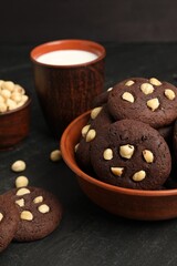 Tasty chocolate cookies with hazelnuts and milk on black table, closeup