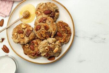 Tasty cookies with nuts, honey dipper and milk on white marble table, flat lay. Space for text