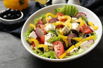 Delicious fresh Greek salad in bowl on black table, closeup