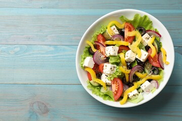 Delicious fresh Greek salad in bowl on light blue wooden table, top view. Space for text