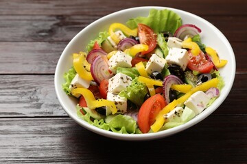 Delicious fresh Greek salad in bowl on wooden table, closeup