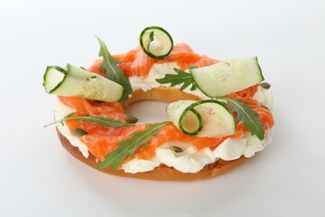 Half of delicious bagel with salmon, cream cheese and cucumber on white background, closeup