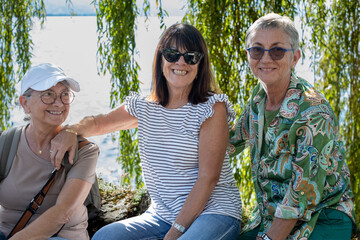 Three very happy mature women hug each other outdoors on a sunny day at Lake Geneva, Tourism, travel, friendship, sharing
