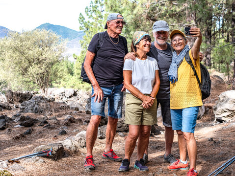 Happy group of senior friends enjoying retirement and adventure trekking in the forest, four elderly people take a selfie smiling. Sport, freedom, healthy lifestyle concept