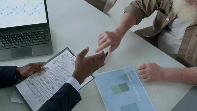 High angle view of senior man with white beard shaking hands with financial advisor after signing contract at office table