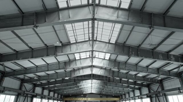 Ceiling of an industrial warehouse or workshop, with a large window. The beams in the roof structure provide strength and rigidity.