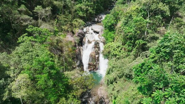 Costa Rica, San Gerardo de Rivas: majestic waterfall plunges through dense jungle canopy, creating dramatic dual streams that merge into turquoise pool below. Aerial perspective, backwards motion.