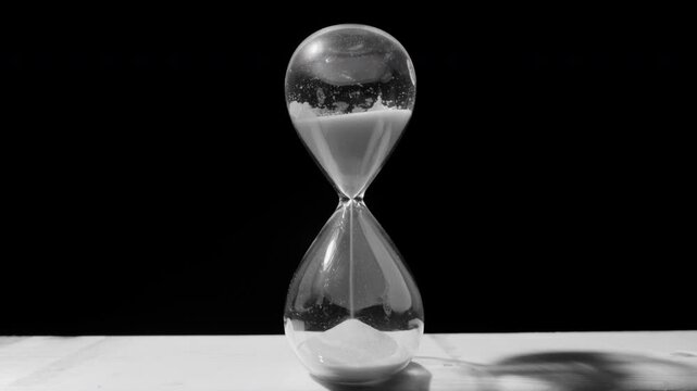 Desaturated arcing shot of sand falling in hourglass, time running out concept