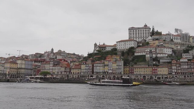 A long boat moving across from right to left on the Douro river with the old town of Porto in the background on an overcast day