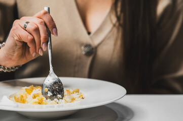 A close-up of a hand holding a spoon, delicately serving rice topped with almond flakes from a white plate. The background features a blurred figure, enhancing the focus on the meal.