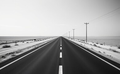 A scenic road winds through a dramatic desert landscape, with towering red rock cliffs and a clear blue sky in the background.