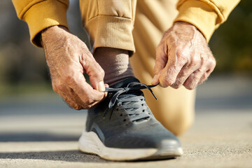 Close up of senior athlete's hands tying shoelace on sneaker outdoors.