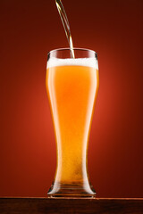 pouring beer into glass, wooden stand, red background, close-up view of object, beer foams and bubbles