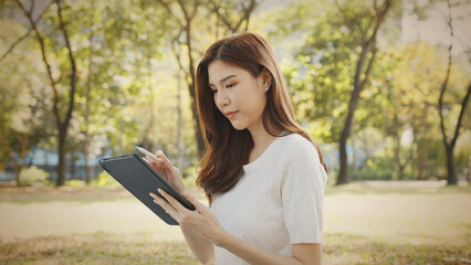 Attractive Freelance Woman Relaxing and Working Remotely in Nature, Happy Female Professional on a Video Call, Tech-Savvy Female Learning Online. Young Woman Reading and Communicating a Tablet