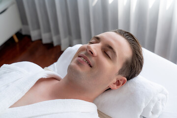 Caucasian man customer enjoying relaxing anti-stress spa massage and pampering with beauty skin recreation leisure in day light ambient salon spa at luxury resort or hotel. Quiescent