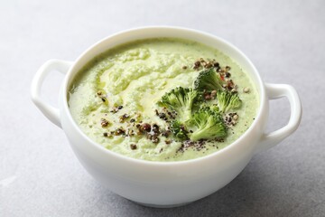 Delicious broccoli cream soup in bowl on light table, closeup