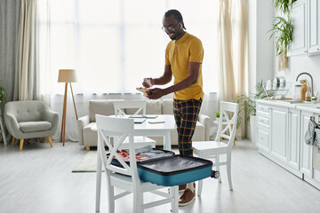 Young man organizes his travel essentials in a bright kitchen setting while working remotely